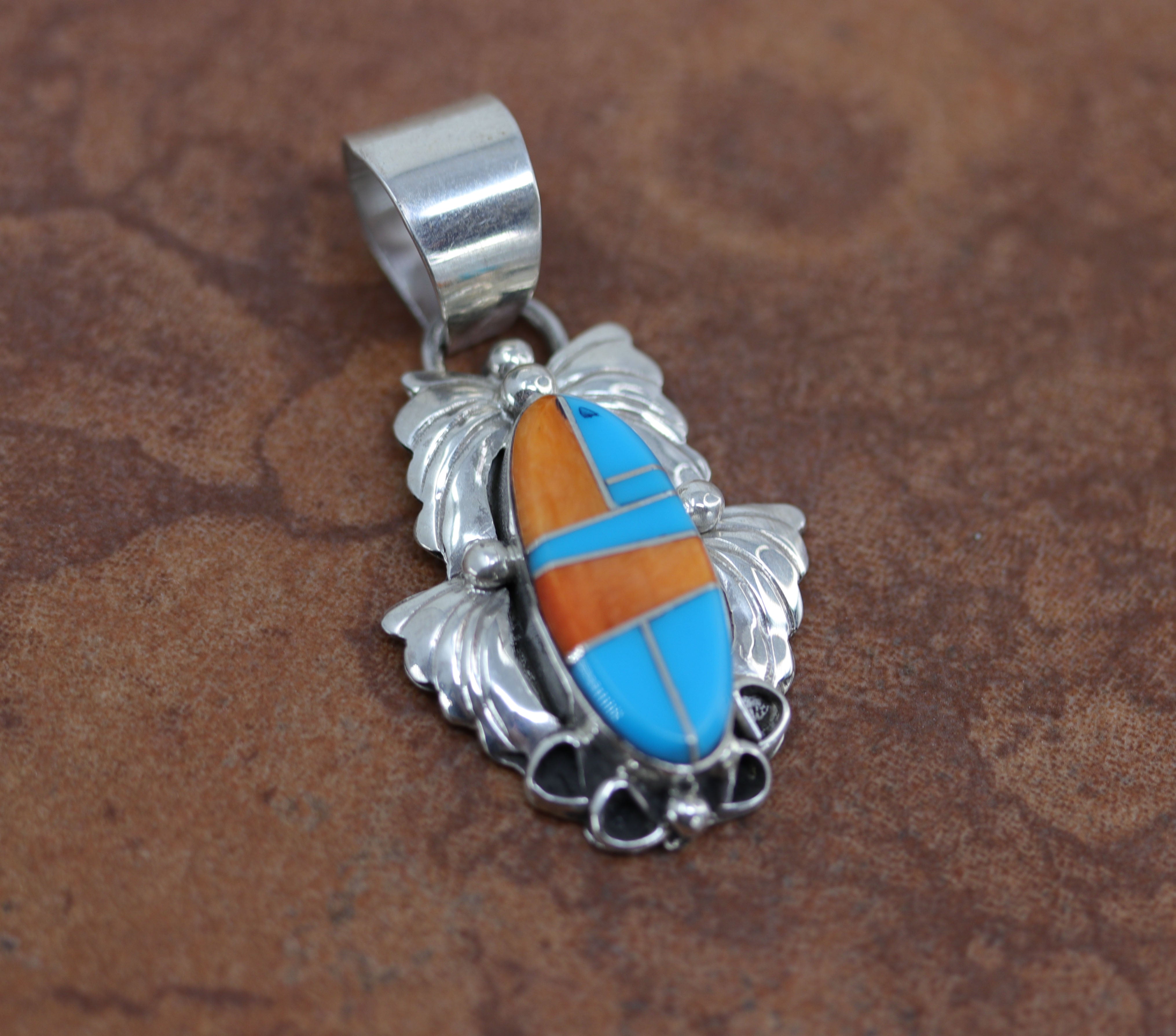 A beautiful Navajo Native American Pendant. It is made from sterling silver and multi-stone inlay. It is 2" long and about 1 1/8" wide.&nbsp;